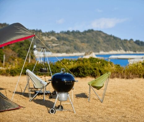 a weber grill in front of the deck chairs and next to the tent